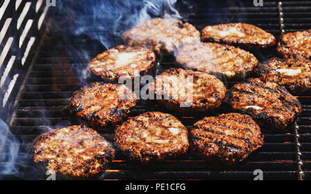 Vorbereitung leckere Hamburger auf dem Grill im Freien für die ganze Familie das Mittagessen. Konzeptionelle Bild der gegrillte Burger bei Feuer Flamme. Hamburger Pastetchen. Stockfoto