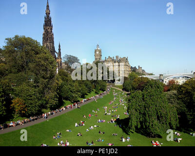 Touristen, Besucher und Einheimische in der Princes Street Gardens an einem heißen und sonnigen Tag in Edinburgh entspannen. Das Scott Monument und Balmoral Hotel sind im Hintergrund. Stockfoto