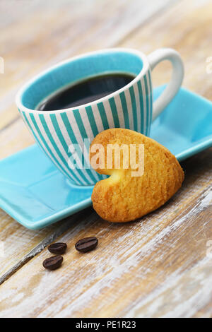 Herzförmige crunchy Cookie lehnte sich gegen blaue Tasse Kaffee auf Holzmöbeln im Landhausstil Oberfläche Stockfoto