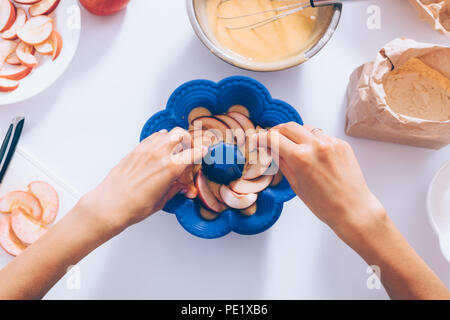 Der weibliche Hände hinzufügen geschnittenes Obst in Auflaufform für traditionelle Apfelkuchen in der Nähe von Zutaten und Küchenutensilien, Ansicht von oben. Frau kochen Saison Herbst Stockfoto