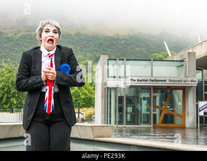 Edinburgh, Schottland, Großbritannien. 12. August 2018. Edinburgh Fringe Festival Fotoshooting auf einem trostlosen schottische Wetter Tag, Schottische Parlament, Holyrood Edinburgh, Edinburgh, Schottland, Vereinigtes Königreich. Politischen Clowns in Silly stellt außerhalb des Parlaments. Schwein Circus ist als 'Verbatim Brexit Parodie' über den Umgang der Regierung mit Brexit Verhandlungen in Rechnung gestellt, mit Charakter Teresa kann vor dem Schottischen Parlament. Durch die Theatergruppe Hitchhiker Kollektive produziert Stockfoto