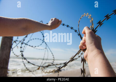 Offene Hände Stacheldraht draußen am Strand. Stacheldraht zum Meer während der sonnigen Tag. Stacheldraht am Strand. Stockfoto