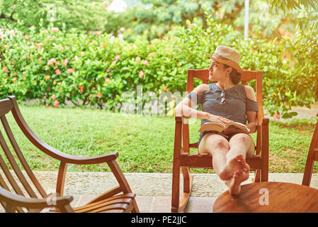 Frau im Urlaub Thema. Lesen buchen Sie im schönen Sommergarten Stockfoto