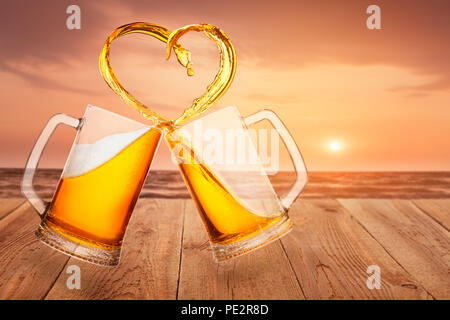 Liebe zu Bier Konzept. Zwei Glas Becher Toasten und Erstellen von Splash in Herzform auf Meer Hintergrund Stockfoto