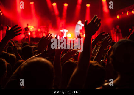 Konzert Masse während Festival, Hände vieler Menschen zujubeln Musiker Musik auf der Bühne, rote Hinterleuchtung Stockfoto