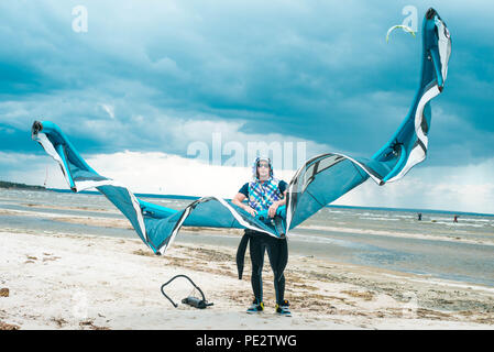 Kitesurfer hält seinen Drachen mit einem Sturm im Hintergrund in einem schönen symmetrischen Porträt. Kite Surfer hält Kite an einem Strand bei stürmischem Wetter Stockfoto