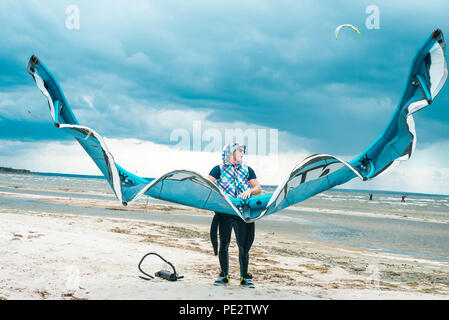 Kitesurfer hält seinen Drachen mit einem Sturm im Hintergrund in einem schönen symmetrischen Porträt. Kite Surfer hält Kite an einem Strand bei stürmischem Wetter Stockfoto