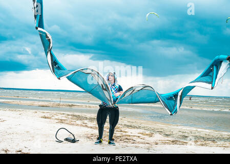 Kitesurfer hält seinen Drachen mit einem Sturm im Hintergrund in einem schönen symmetrischen Porträt. Kite Surfer hält Kite an einem Strand bei stürmischem Wetter Stockfoto