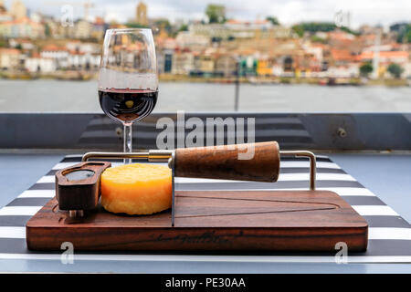 Gläser Portwein und ein kleines Rad der Käse auf dem Board auf ein Restaurant im Freien mit den Fluss Douro und Dom Luis I Brücke verschwommen im Hinterg Stockfoto