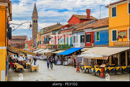 Burano, Italien, 25. September 2017: malerische Fußgängerzone mit Geschäften, Restaurants und bunten Häuser und eine Kirche im Hintergrund, in der Buran Stockfoto