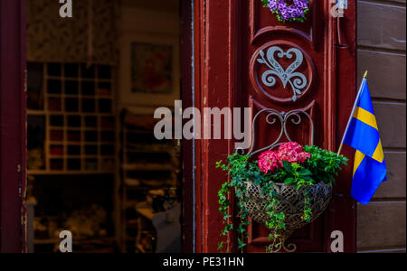 Reich verzierte rote Tür an einem Souvenirshop mit einem schwedischen Flagge und einem Blumentopf in Gamla Stan, der Altstadt von Stockholm, Schweden eingerichtet Stockfoto