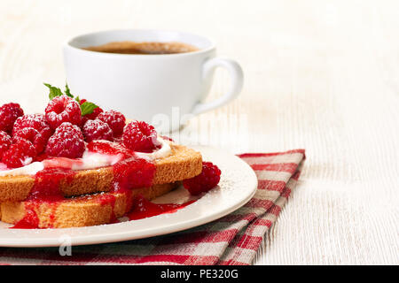 Toast mit Frischkäse und Himbeeren über textile Serviette auf weiße Holztisch Stockfoto