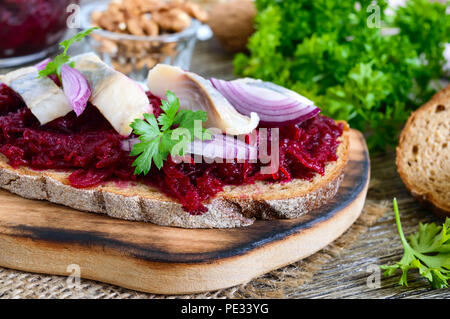 Geriebene gekochte rote Rüben, Stücke von Hering, roten Zwiebeln, Nüsse auf Vollkornbrot. Leckere und gesunde Sandwich. Die richtige Ernährung. Stockfoto