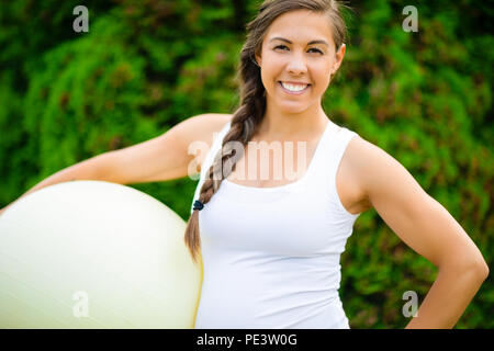 Lächelnde junge schwangere Frau mit Fitness Ball im Park Stockfoto