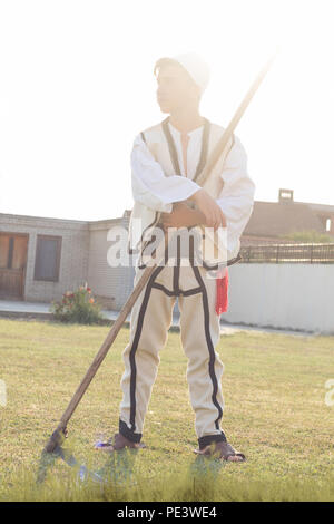 Junge Mann in traditioneller Tracht das Gras mit der Sense in der alten Weise mähen Stockfoto