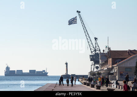 THESSALONIKI, Griechenland - 25 Dezember, 2015: die Menschen entspannen auf den Kai - Pier auf den alten Hafen von Thessaloniki, eine griechische Flagge und ein frachtschiff können Se werden Stockfoto