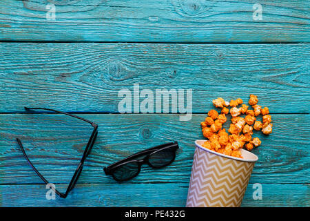 Pappbecher mit Popcorn und 3D-Brille auf blauem Hintergrund. Ansicht von oben. Stockfoto