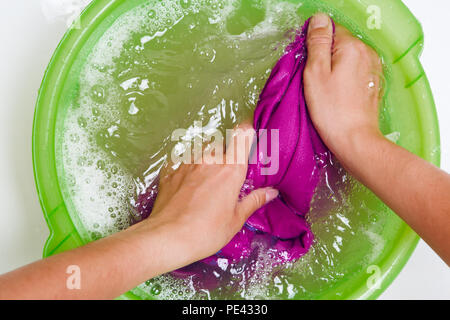 Foto oben von Frau Hände waschen violette Kleidung in grünen Becken Stockfoto