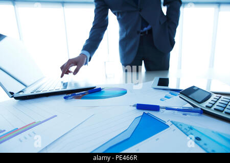 Unternehmer im Büro durch Drücken der Taste am Laptop, finanzielle Daten, Unterlagen auf dem Tisch Stockfoto