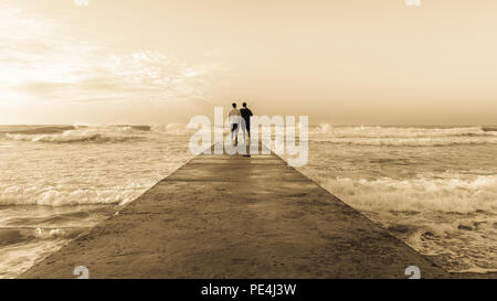 Vater Sohn angeln silhouetted unbekannter am Strand Steg Waters Edge mit Wellen am frühen Morgen blaue Himmel Landschaft. Stockfoto