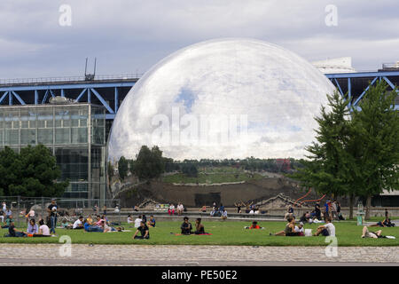 Paris Park - Menschen entspannend auf Gras der Park La Villette mit Blick auf Spiegel- dome La Géode, Paris, Frankreich, Stockfoto