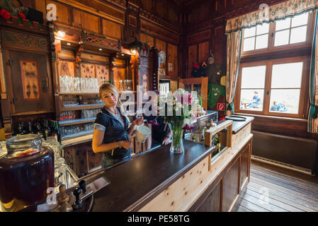 Blonde Frau mit Zopf hinter der Theke in der herrlichen Speisesaal der Berghütte Berliner Hütte lächeln in die Kamera, Zillertal, Österreich Stockfoto