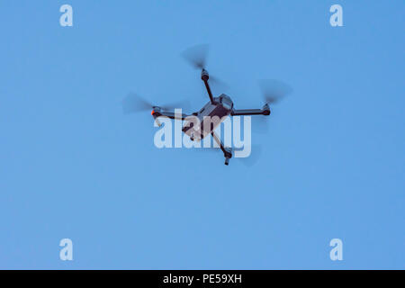 Schwarz Kamera Drohne im Flug mit sichtbaren Propeller Bewegung und Blitzleuchte und blauer Himmel. Stockfoto