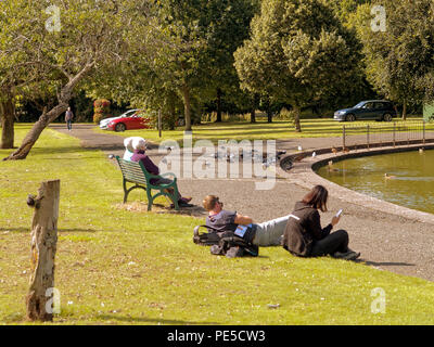 Knightswood park Pond Park leben sonnigen Sommertag Leute sitzen mit heißem Wetter Stockfoto