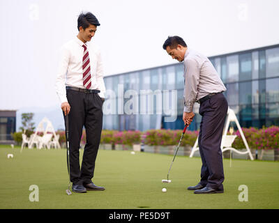 Zwei asiatische Geschäftsleute entspannen und spielen Golf auf dem Dach. Stockfoto