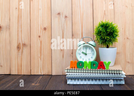 Montag Buchstaben text und Notebook Papier, Wecker und wenig Deko Baum in weiße Vase auf hölzernen Hintergrund, hallo Montag Konzept Idee. Stockfoto