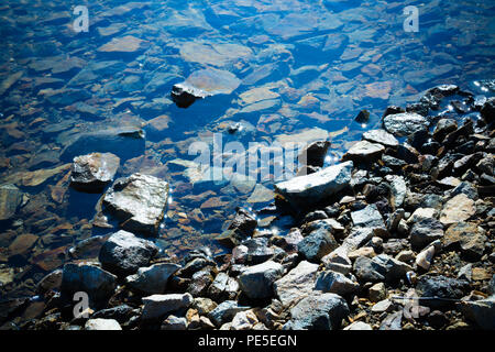 Felsige Ufer mit reflektierenden Wasser in der Sonne. Stockfoto