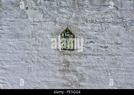 Stuck bedeckt alten Ziegelmauer mit Bleiglas anzeigen Bullauge durch den Heilpflanzengarten hinter der Wand. Bullauge in Form von Haus. Stockfoto