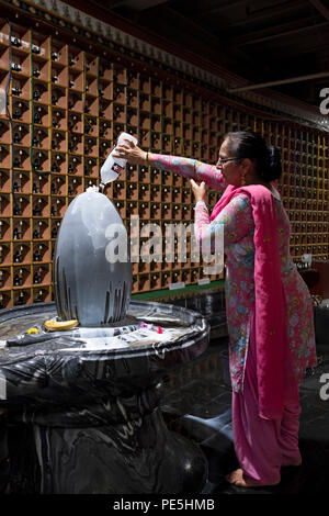 Eine Hindu-Frau gießt Milch über eine Statue des diessigen Shiva in einem Hindu-Tempel in Woodside, Queens New York City. Stockfoto