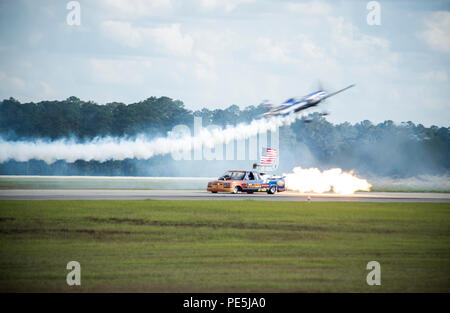 Ein Kunstflugzeug der MXS führt eine Flugdemonstration über dem Flash Fire Jet Truck beim Thunder Over South Georgia Open House auf der Moody Air Force Base, Georgia, durch. Die MXS ist ein einmotoriges Hochleistungs-Kunstflugzeug, das von einem Lycoming AEIO-540-Triebwerk angetrieben wird. Der Flash Fire Jet Truck kann Geschwindigkeiten von bis zu 400 km/h erreichen. Die Demonstrationen beleuchten Präzisionsflugzeuge, die Flugsteuerung und die Koordination mit bodengestützten Displays für öffentliche Interaktionen. Stockfoto