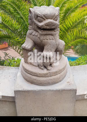 Alte chinesische Kaiser lion Statue auf einem Sockel aus Stein im Hintergrund schöne grüne Palmen eine Finca mit Pool. Stockfoto
