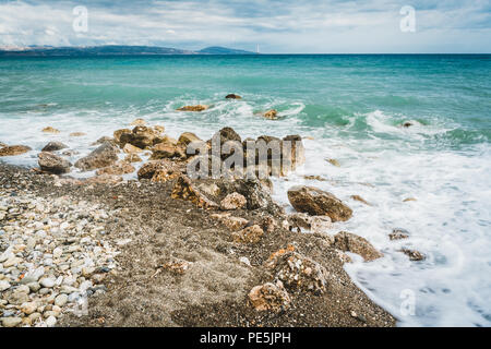Wellen schlugen gegen Steine an einem sonnigen Tag auf Kreta, Griechenland. Blaue Meer Ozean im Hintergrund und Stein Strand im Vordergrund. Foto in Griechenland. Stockfoto