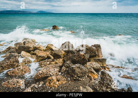 Wellen schlugen gegen Steine an einem sonnigen Tag auf Kreta, Griechenland. Blaue Meer Ozean im Hintergrund und Stein Strand im Vordergrund. Foto in Griechenland. Stockfoto
