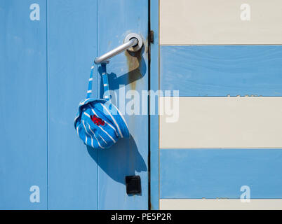 Blau und Weiß Gestreifte Mütze Kind mit einem roten Krabbe detail, hängen an der Tür in der einen und einem blau-weiß gestreiften Beach Hut mit einer blauen Tür Stockfoto
