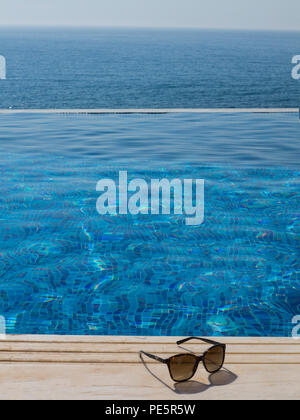 Sonnenbrille auf Holzterrasse durch ein Infinity Pool Stockfoto