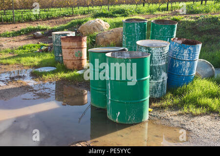 Eine Gruppe von leeren Industrial Metal Schlagzeug Farbe bespritzt und sitzen in einer Pfütze von Wasser und auf das Gras an einem Weinberg Stockfoto