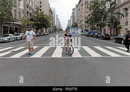 Washington D.C., USA. 12 August, 2018. Eine Frau steht hält Ihr Fahrrad an der Kreuzung von der 14th Street NW und F Street NW holiding ein Schild mit der Aufschrift "Liebe". Außerhalb der Rahmen ist das counterprotest März protestieren die 'Vereinen das Recht 'alt-rechts Rallye so Marchers sie sah, als sie ihre biegen Sie an der Kreuzung. Credit: Mark Kanning/Alamy leben Nachrichten Stockfoto