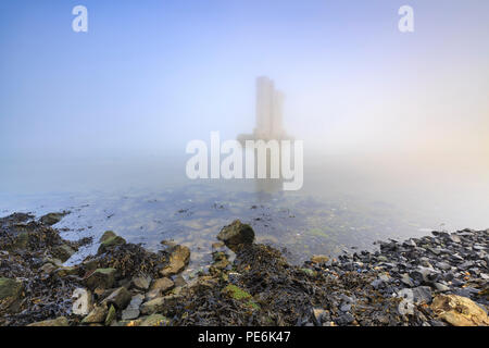 Einer der verbleibenden Säulen der Sturmflutwehr stehend im Wasser während eines schweren dichten Nebel im Winter Sonnenuntergang an der Deltawerke Sturmflut Meer Stockfoto