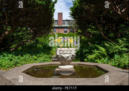 Brunnen mit einem Herzstück der Stiefmütterchen in einem Stein Pflanzmaschine. Ein Herrenhaus im georgianischen Stil in einem formalen Garten. Das Anwesen wird oft für Hochzeiten genutzt Stockfoto