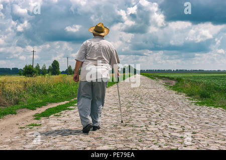 Älterer Mann mit geht walking stick tragen Strohhut home auf einer gepflasterten Straße, im Zentrum der Ukraine Stockfoto