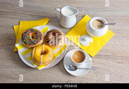 Drei Donuts auf einem Teller, kleine Tasse Kaffee, Kanne, Milch und Zucker Topf auf Tischplatte. Stockfoto