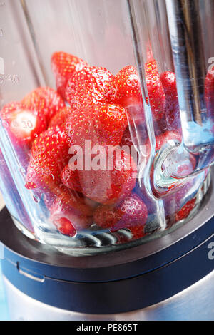 Geschälte reife Erdbeeren in einen Mixer auf einem blauen Holztisch Stockfoto