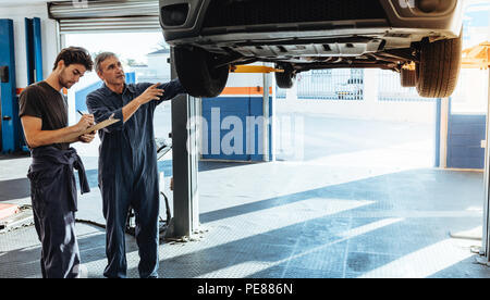 Zwei Automechaniker in Uniform die Prüfung des Auto- und Notizen für die Reparaturen durchgeführt werden. Mechaniker, Liste der Auto Fehlfunktionen. Stockfoto