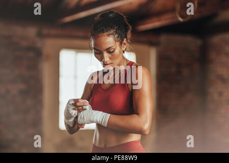 Weibliche Boxerin trägt Armband am Handgelenk. Fitness-junge Frau mit muskulärem Körper, die sich auf das Boxtraining im Fitnessstudio vorbereitet. Stockfoto