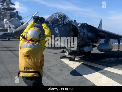 Aviation Boatswain’s Mate (Handling) 2nd Class signalisiert einen AV-8B Harrier Piloten auf dem Flugdeck der USS Boxer (LHD 4) am 23. Oktober 2015 während einer Composite Training Unit Exercise (COMPTUEX). Die Boxer Amphibious Ready Group, einschließlich USS New Orleans (LPD 18), USS Harpers Ferry (LSD 49) und der 13th Marine Expeditionary Unit, führt szenariogesteuerte Übungen durch, die Schiffe und Marines integrieren, um die Einsatzbereitschaft, Koordination und kombinierte Fähigkeiten zu verbessern. Stockfoto