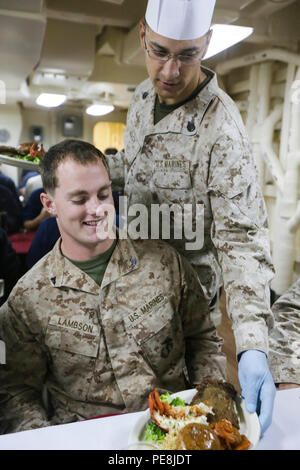 Golf von ADEN (29. Oktober 2015) US Marine Staff Sgt. James Leach, Recht, dient CPL. Cody Lambson seine Mahlzeit der Oktober Geburtstag Abendessen an Bord der USS Anchorage (LPD-23).  Lauge ist ein Zug-Sergeant mit Battalion Landing Team 3. Bataillon, 1. Marineregiment, 15. Marine Expeditionary Unit und Lambson ist ein Scout mit dem 15. MEU Force Reconnaissance Detachment.  Marines und Matrosen feiern ihren Geburtstag für den Monat Oktober mit einem Steak und Hummer Schweif Abendessen durch ihre Mitarbeiter Unteroffiziere gedient.  Die 15. MEU eingeschifft auf den Schiffen der Essex amphibische bereit Gr Stockfoto